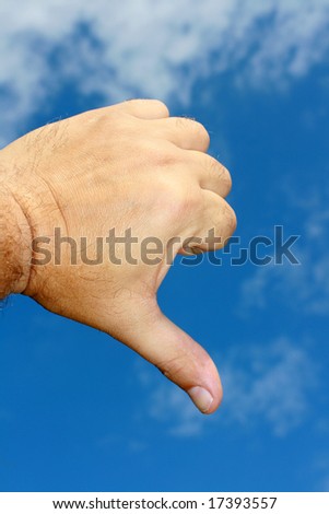 A hand gesture. A male hand making the gesture of thumbs down. Set on a blue sky background.