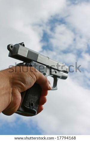 A hand held gun with trigger pulled held in the hand set against a sky backdrop
