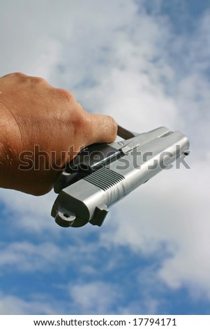 A hand gun pointed upwards towards a sky background