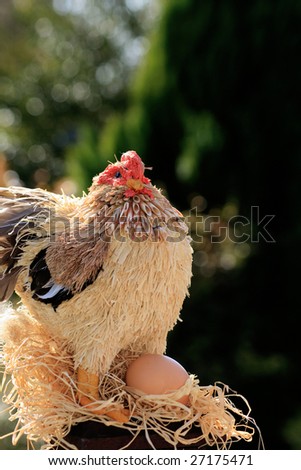 A hand made straw and string constructed chicken/rooster perched atop a wooden post with an egg.