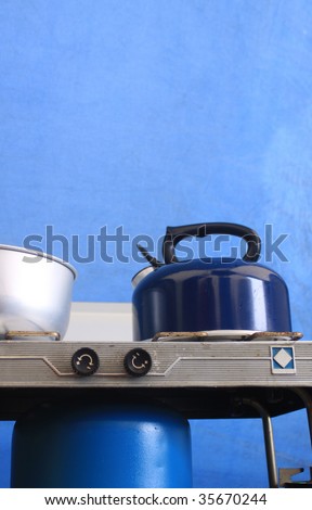 A blue kettle on top of a camping gas stove, set against a blue canvas tent background.