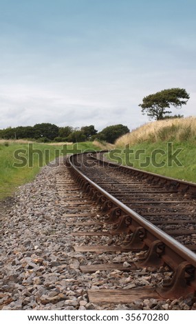 A low angled image of steel railway tracks and wooden sleepers. Track curves at the mid horizon point around a corner. Location is on the Swanage Steam Railway Network in Dorset, UK.
