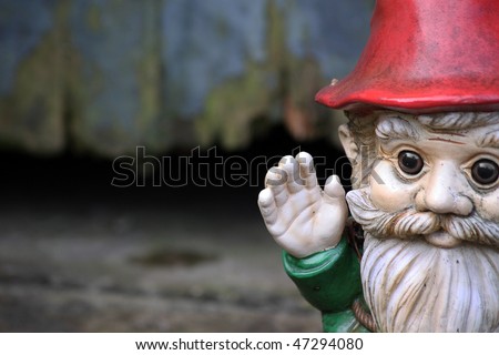 A bearded garden gnome on a landscape format set to the right of the image waving his hand. Set against a wooden garden shed door.