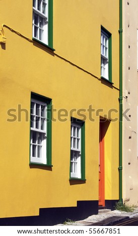 The brightly painted yellow frontage of a coastal cottage. Located in the coastal town of Lyme Regis in Dorset, England. Window frames painted in bright green, with a vivid orange painted door.