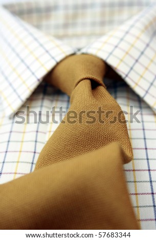 A close up view of a mans cotton checked shirt with a matching mustard coloured woollen tie. Low angled view with focus to middle.