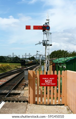 A period railway signal at the end of the platform at Harmans Cross station, part of the Swanage steam railway network in Dorset. Period railway carriages are visible in the background.