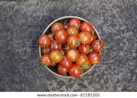 A single bowl of small round shaped red tomatoes in a brown ceramic bowl shot from above.
