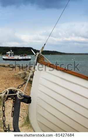 The bow, or front, of a small white wooden boat or dinghy. Detail of the bow with its tethered ropes to the shore.