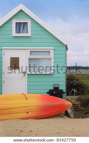 A colorful green wooden beech hut with an orange and yellow surf board resting in the sand to the front of the hut. Located in the South of England at Christchurch, Dorset, England.