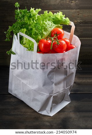 Shopping back full of vegetables in wooden background.