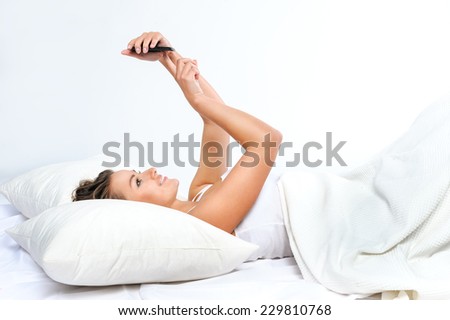 Young woman in looking at mobile phone while lying in bed