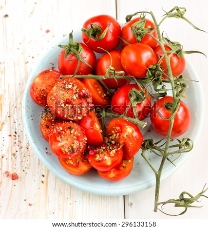 Fresh grape tomatoes with coarse salt for use as cooking ingredients with a halved tomato in the foreground over wooden background