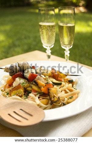 A romantic outdoor meal with grilled vegetable linguine and champagne.