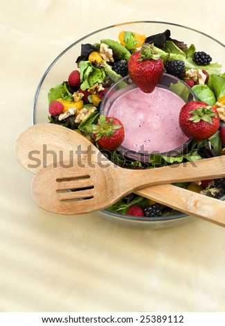 A bowl of berry field greens with yogurt dip and wooden serving spoons.