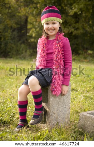 A five-year-old girl sitting in  the grass on a cement block