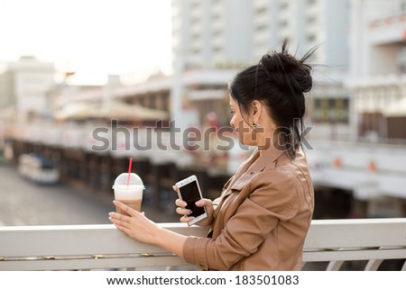 A beautiful woman checking email on the mobile phone and holding a cup of take away coffee.