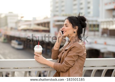 A beautiful woman checking email on the mobile phone and holding a cup of take away coffee.