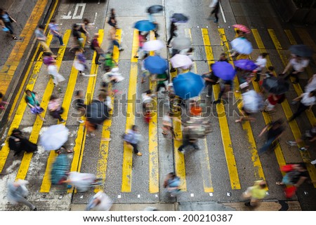 Motion blurred pedestrians crossing Hong Kong street in the rain