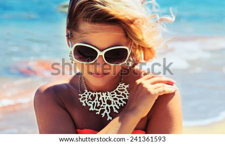 Fashion blonde female in vacation. Posing with cute summer style, pare on bikini, sunglasses and big white necklace