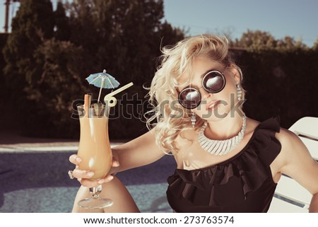 Fashion beautiful woman sunbathing on a chaise lounge with fresh orange juice in luxury pool. Vogue style