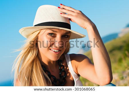 portrait of the attractive, slender, beautiful young Caucasian  blonde girl. Smiling girl enjoys fine warm sunner weather highly in mountains against the sea