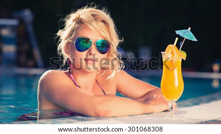 beautiful blonde enjoys in the fine afternoon, lying also the luxury pool, hot summer. girl drink fresh orange juice, slim tanned body,  thin nose