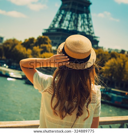young attractive woman in hat, white dress, red bag poses in front of the Eiffel Tower in Paris. Photo with instagram style filters