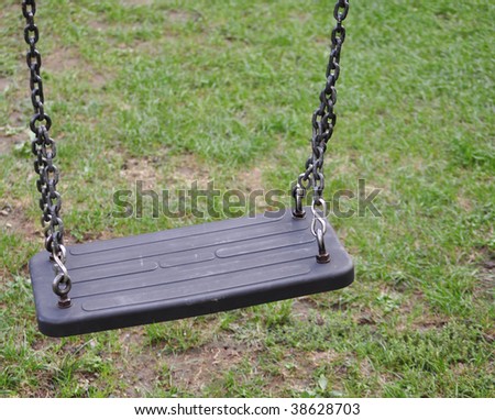 A swing suspended on chains in a playground on the grass