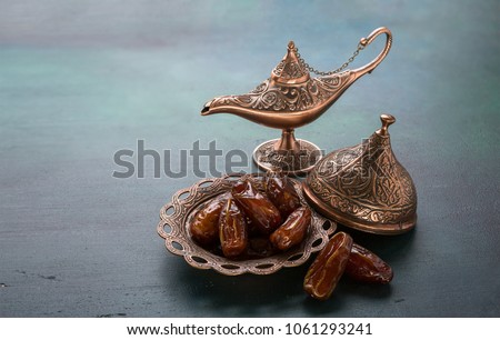 Bronze plate with dates  and aladdin lamp on dark green wooden background. Ramadan background. Ramadan kareem.