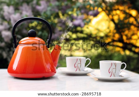 Orange teapot that contains smoking hot tea in front of a blurred background