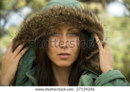 A beautiful woman raises her fur-lined parka to see better.