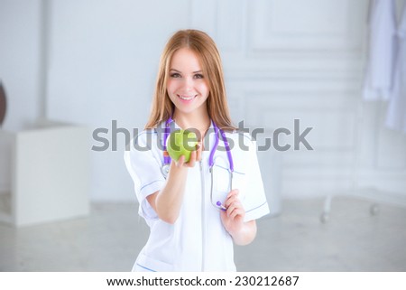 Portrait of a smiling nurse in front. Nurse holding a green apple in the hospital. Concept of healthy food