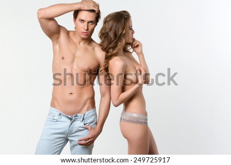 Nude man and woman standing side by side. Woman covers breasts with hand on white background