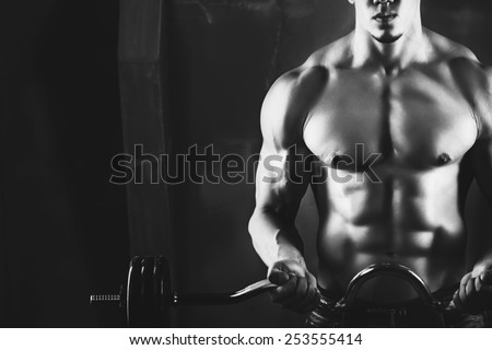 Close up of young muscular man lifting weights over dark background. black and white photo