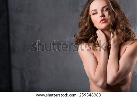 Portrait of sexy woman with curly hair. Posing looking at the camera and closes the chest with his hands. Beauty and fashion.