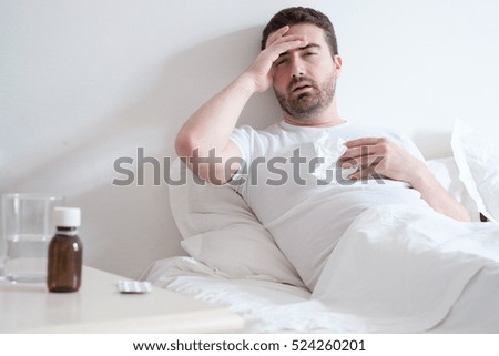 Man feeling cold, lying in the bed and blowing his nose