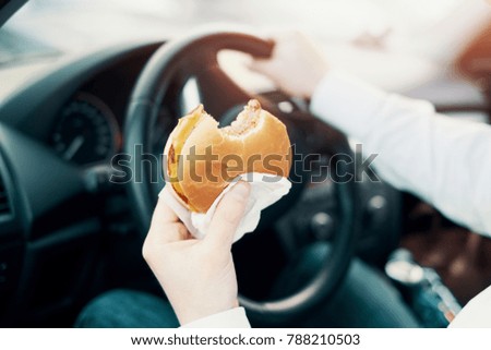 Man eating an hamburger and driving seated in his car