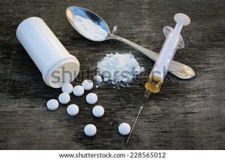 White pill, syringe and heroin on spoon on the old wooden background. Drug addiction.