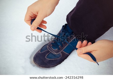 A young man tying shoelaces in sneakers on the background of snow. Toned image.