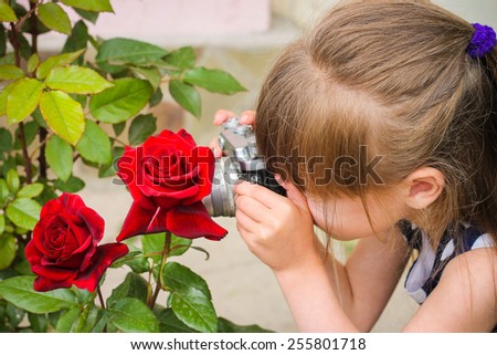 Girl taking photographs with vintage camera. Child photographs of the flower rose.