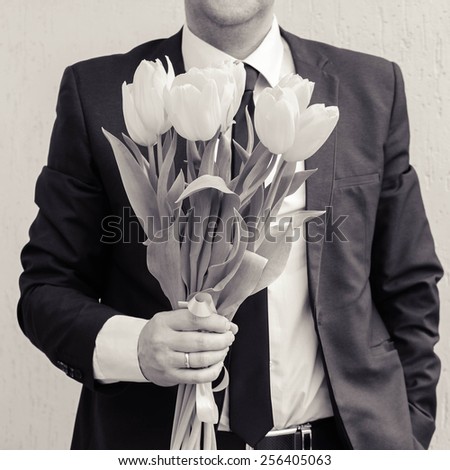 A man wearing a business suit, holding a bouquet of tulips. The man gives a bouquet of flowers. Black and white shot.