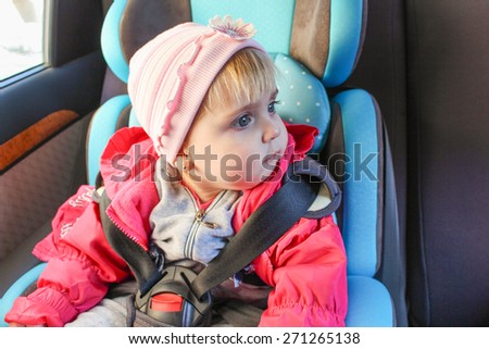 little girl sits in the car seat. The child looks to the side.
