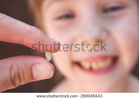 At 6 years old child has lost the baby tooth.   The girl is holding the tooth in his hand.