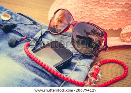 Summer women\'s accessories: red sunglasses, beads, denim shorts, mobile phone, headphones, a sun hat. Toned image