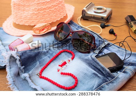 Summer women\'s accessories: red sunglasses, beads, denim shorts, mobile phone, headphones, a sun hat, camera, nail polish, perfum. Toned image