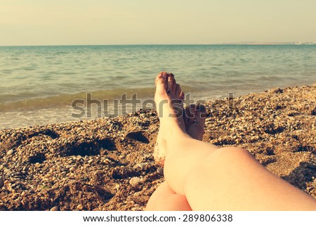 Female feet on the blue sea background. A woman sunbathes on the beach. Girl taken pictures of her feet self. Toned image.