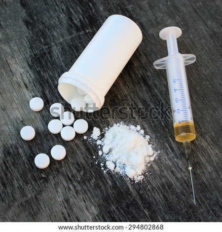 drug addiction on the old wooden background. White pill, syringe and heroin.