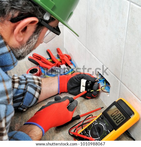 Electrician technician with gloves and safety instruments fixes the electric cable to the socket of a residential installation.