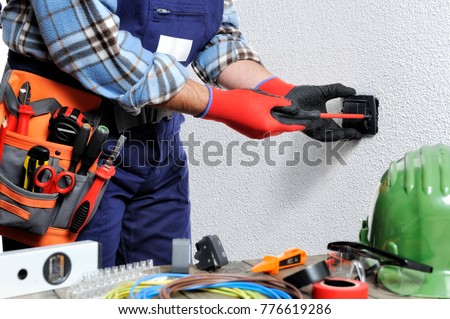 Electrician with hands protected by gloves and insulated tools works on a residential electrical installation.