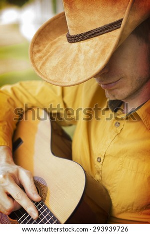 Handsome cowboy in western hat playing guitar